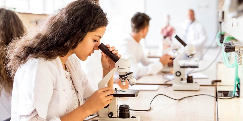 A student looking into a microscope while earning her biology degree in CT